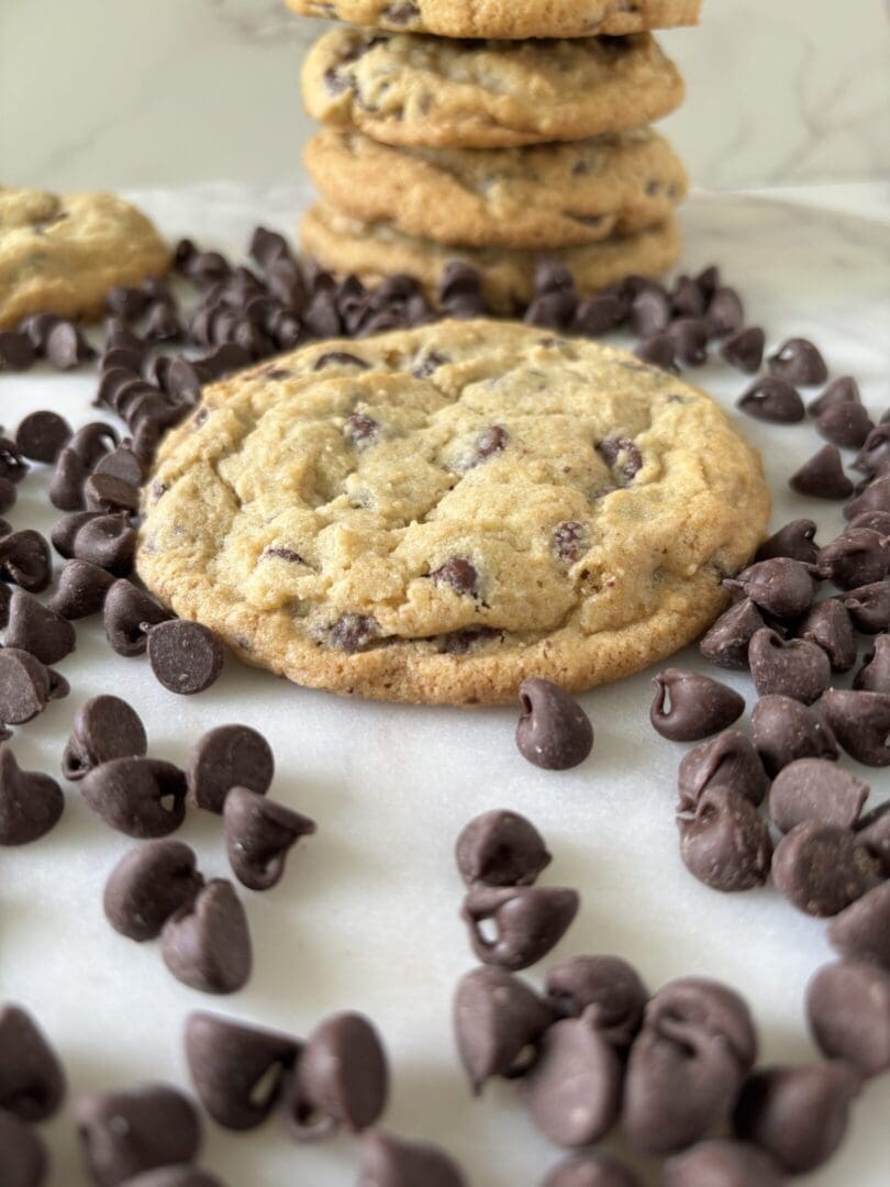 Fresh chocolate chip cookie surrounded by scattered chocolate chips.