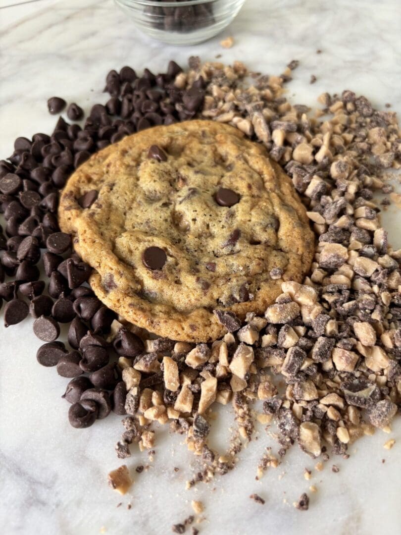 Two chocolate chip cookies surrounded by chopped and whole chocolate pieces.