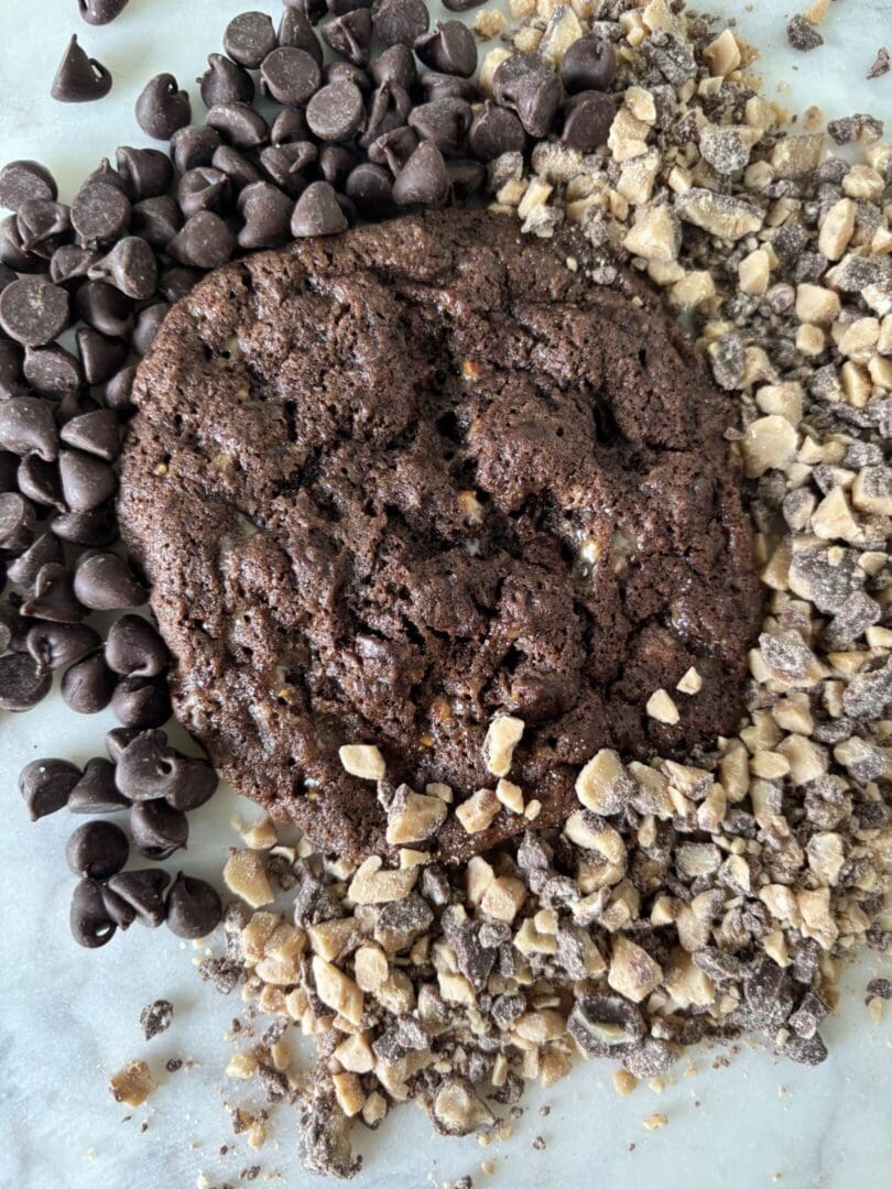 A chocolate cookie surrounded by chocolate chips and chopped nuts.