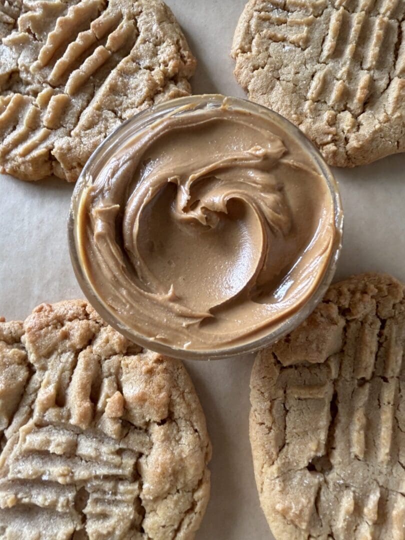 Creamy peanut butter in a bowl surrounded by peanut butter cookies.