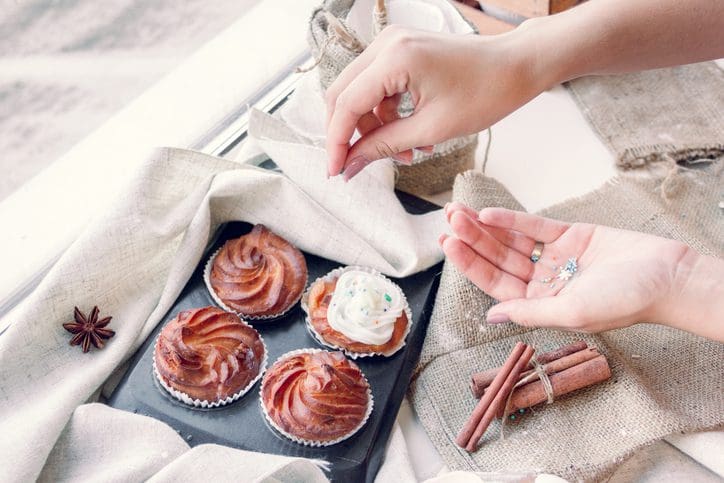 Cupcakes on tray with hands decorating.