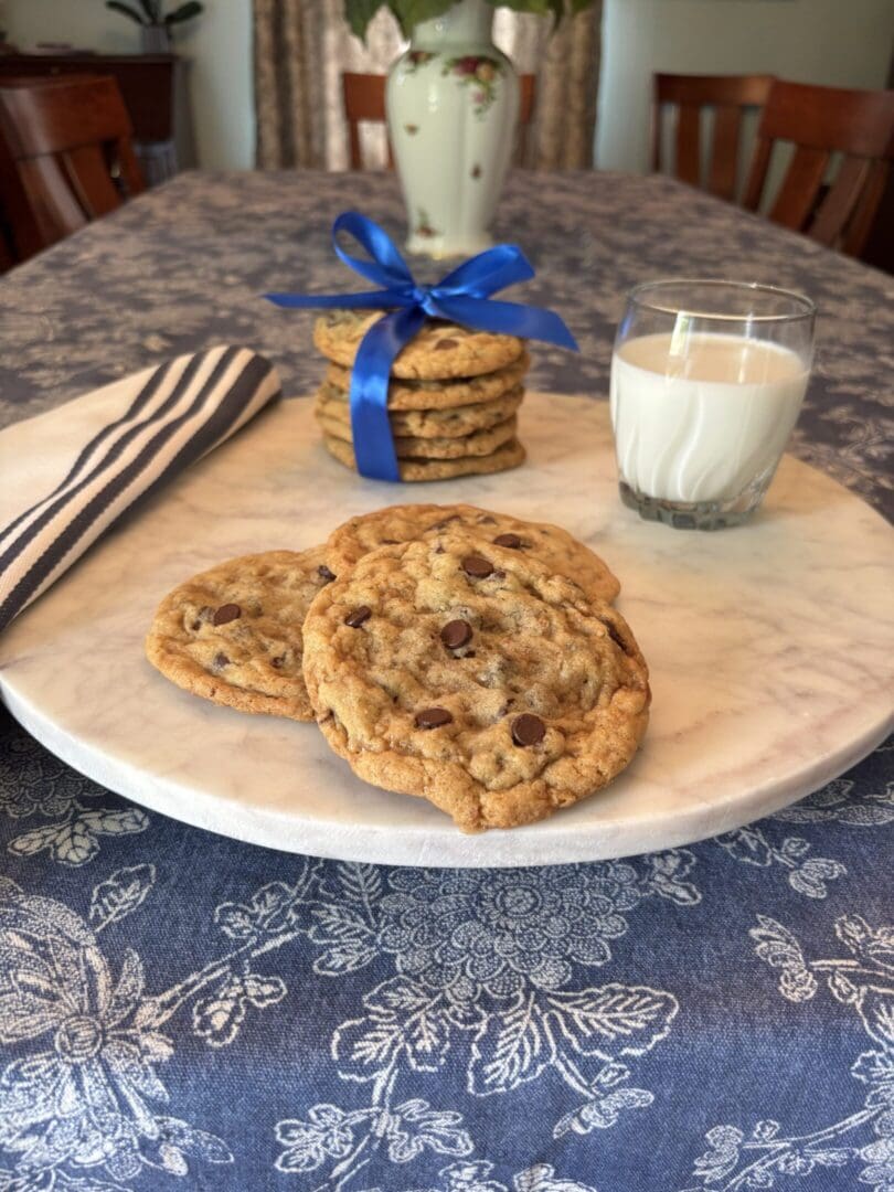 Two chocolate chip cookies on a plate with a glass of milk and a jar of cookies.