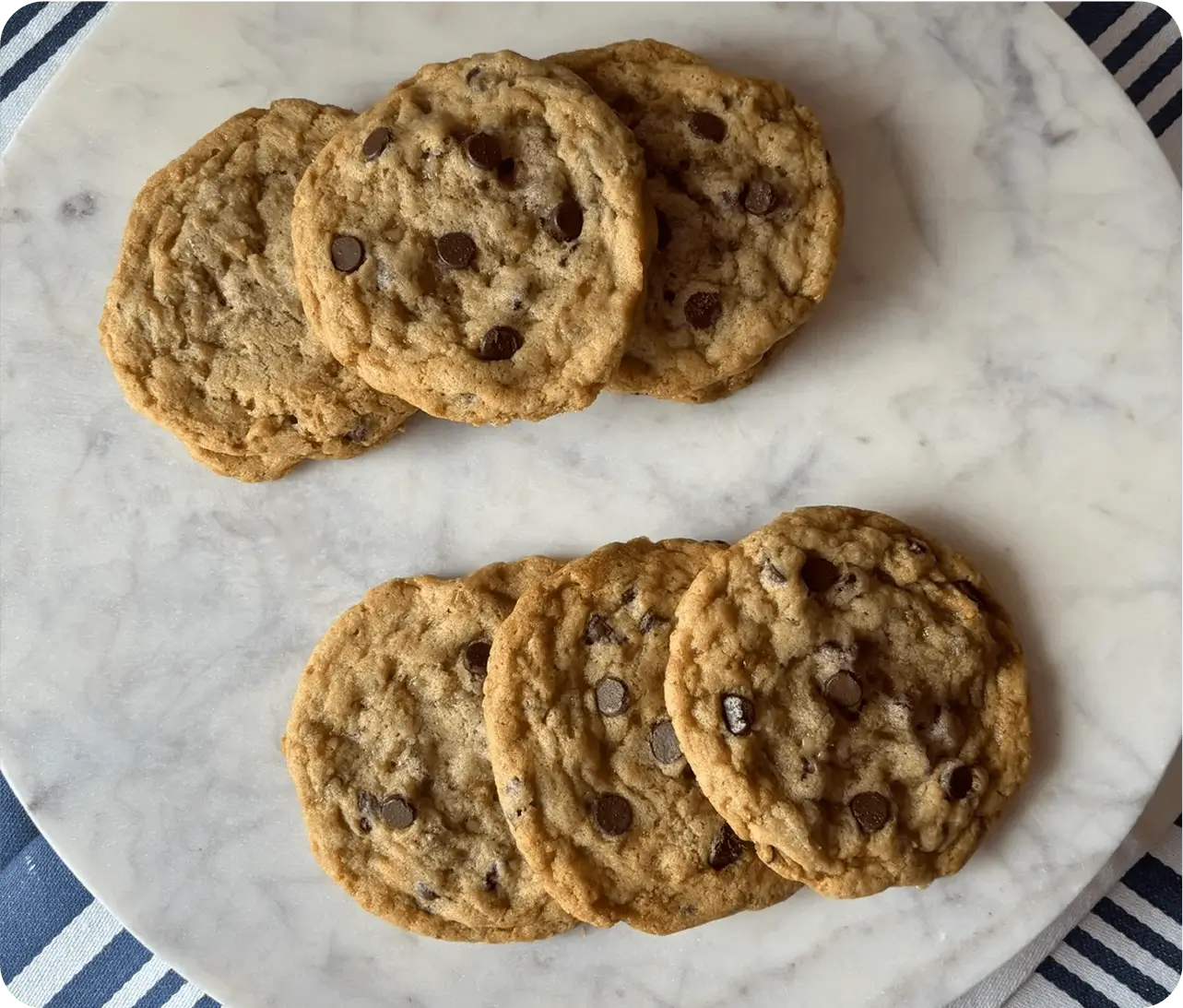 Two stacks of chocolate chip cookies on a marble surface.