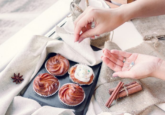 Cupcakes on tray with hands decorating.